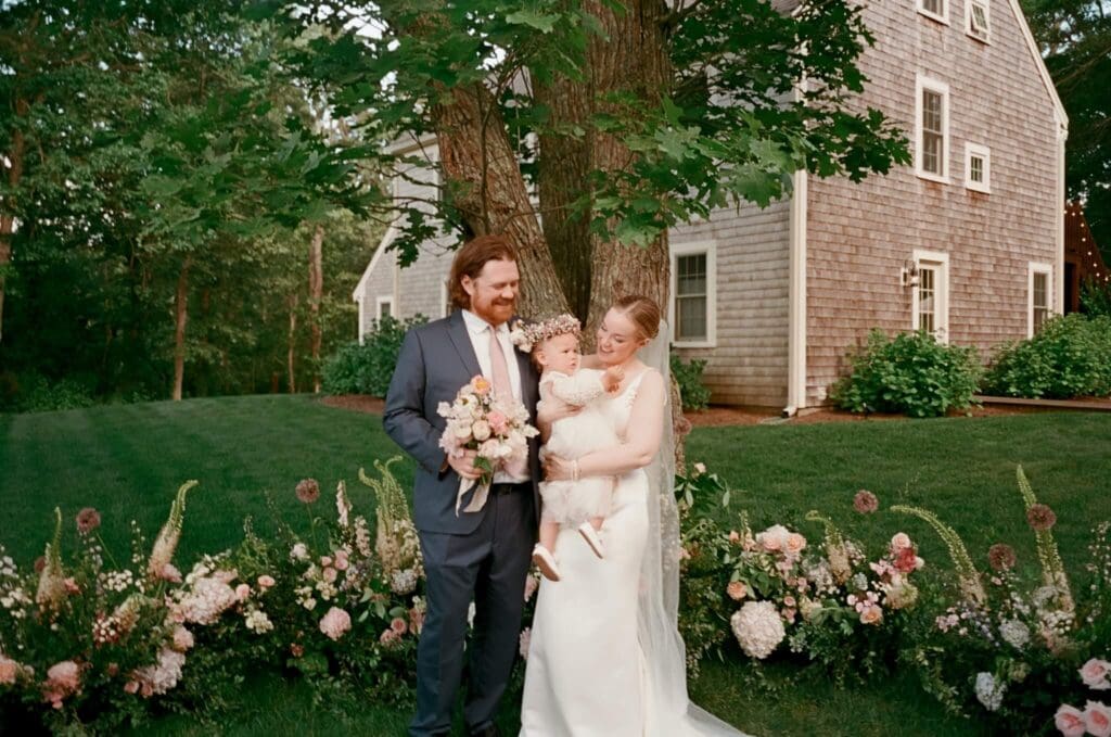 Bride and groom standing with their baby during a small backyard wedding ceremony on Cape Cod