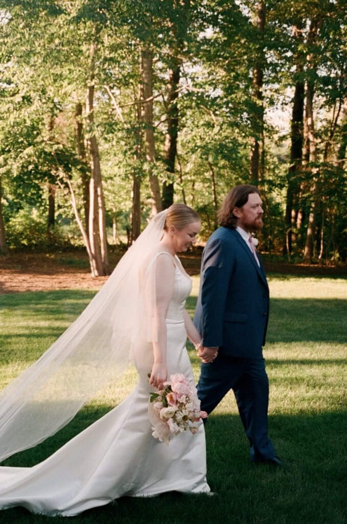 Bride walking across a shaded lawn with groom before a small backyard wedding ceremony