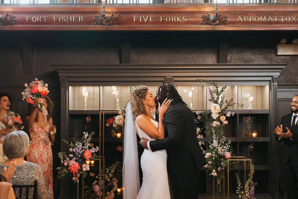 Bride and groom kiss while guests cheer in a dramatic Boston wedding ceremony space