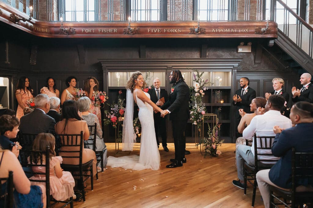 Indoor ceremony with couple standing beneath a floral arch surrounded by candlelight and coordinated bloom