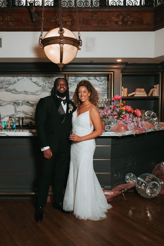 Couple smiling at the bar with cohesive wedding flowers and disco balls styled on the counter