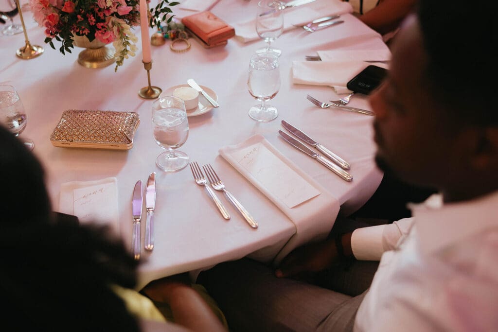 Reception table with printed menus, taper candles, and delicate cohesive floral touches in soft lighting