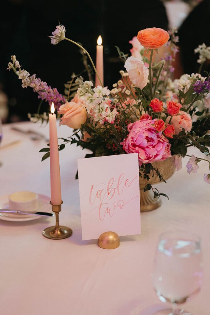 Reception table with taper candles and a garden-style arrangement in pinks and peaches
