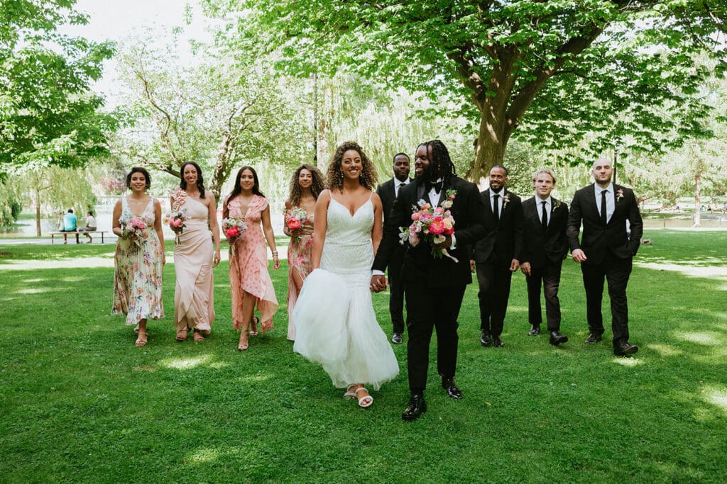 Bridal party walking together through a sunny park, florals and attire styled in soft, cohesive tones