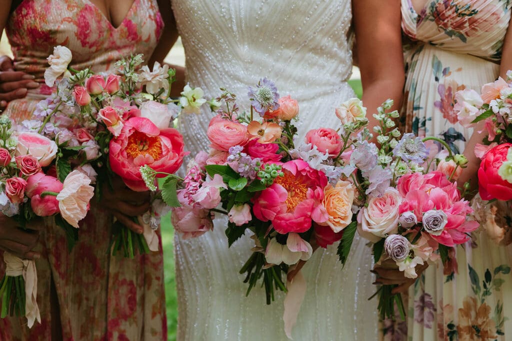 Bride and bridesmaid bouquets with vibrant, movement-filled blooms in bold pink, coral, and peach hues