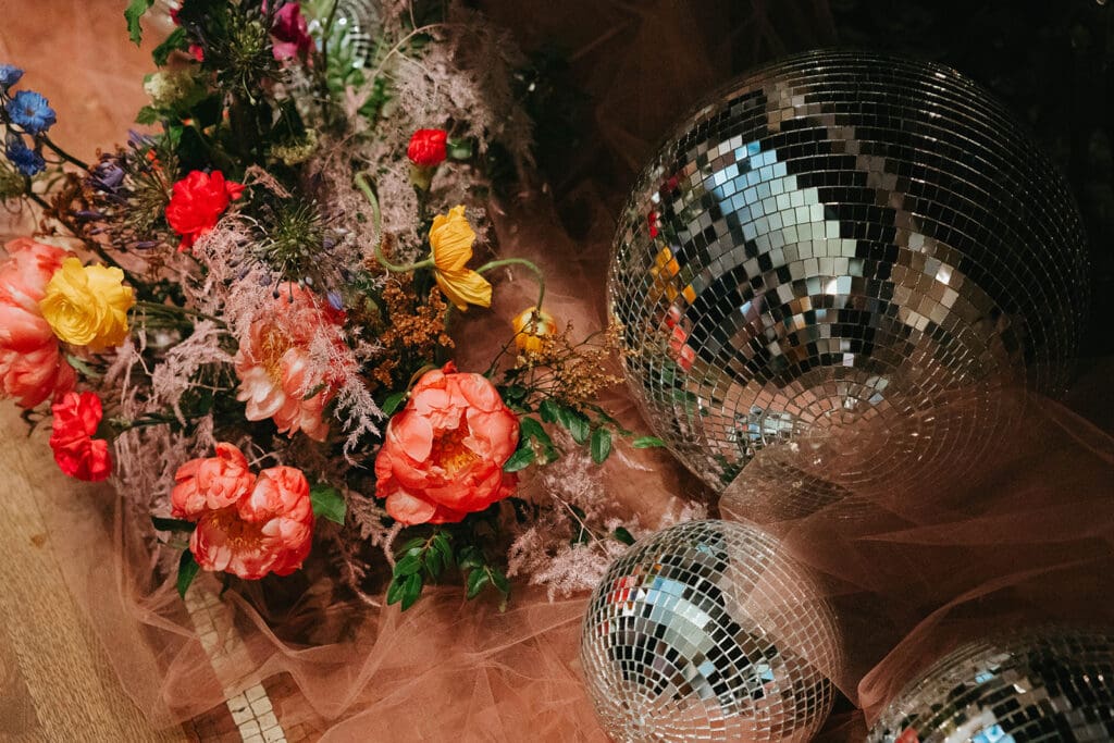 Bright and playful wedding floral installation with coral peonies, yellow ranunculus, and disco balls styled over blush tulle