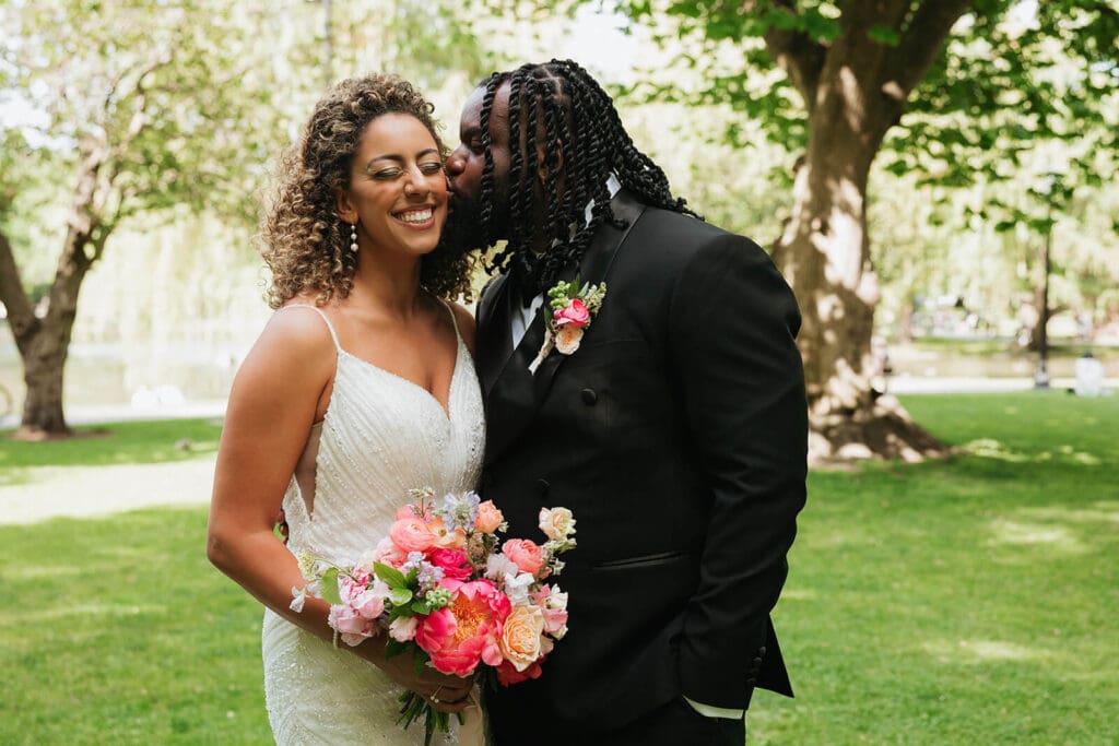 Bride and groom smiling during portraits, bride holding a vibrant bouquet designed with cohesive wedding flowers in coral, peach, and blush
