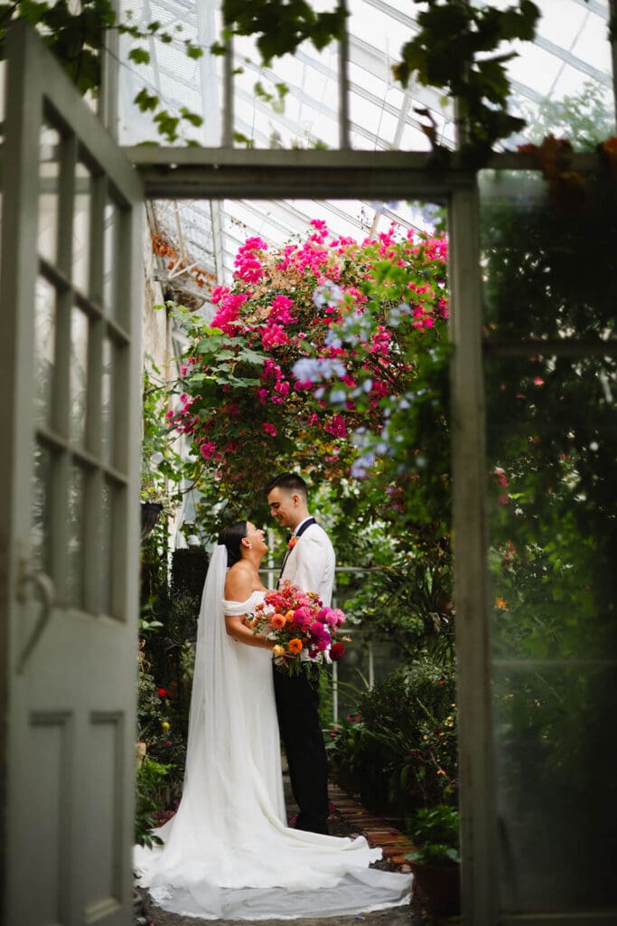 Couple sharing a quiet moment inside the Lyman Estate greenhouse, surrounded by summer wedding flowers and climbing vines.