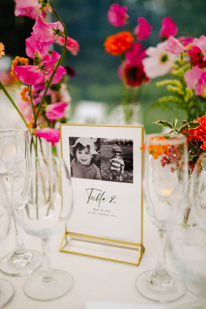 Close-up of a table number sign framed by hot pink sweet peas and orange blooms in delicate bud vases.