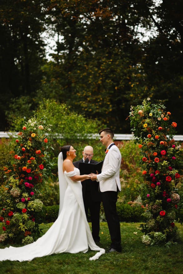 Wedding ceremonyunder twin floral pillars filled with rich, colorful summer wedding flowers.