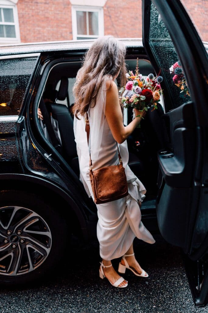Bride stepping into a black car, bouquet in hand, after her city wedding