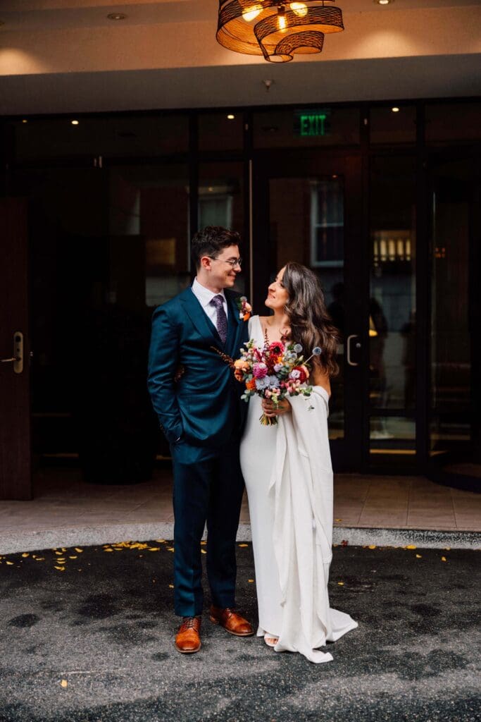Bride in a white dress smiling at groom while holding a textured fall wedding bouquet