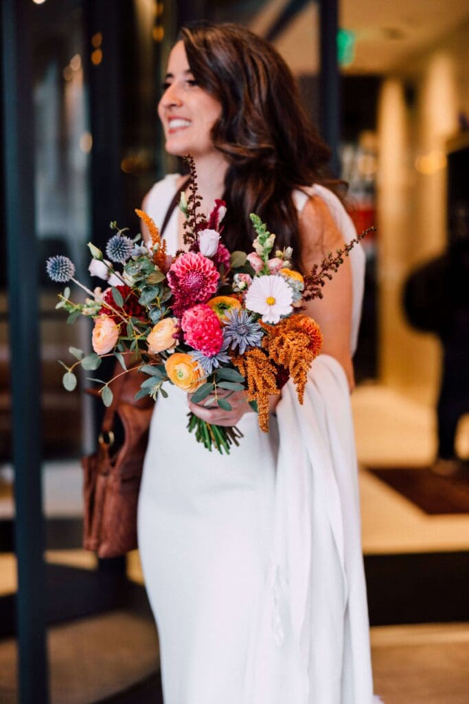Bride holding fall wedding bouquet filled with marigold, berry, and rust tones