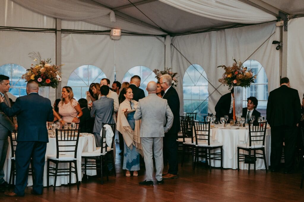 Guests mingling under the tent during a reception with repurposed florals from the ceremony decor