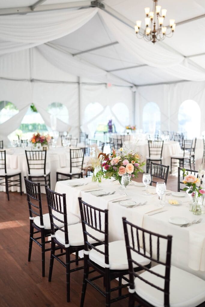 Reception tent featuring a floral-filled cake table and guest tables adorned with repurposed wedding flowers