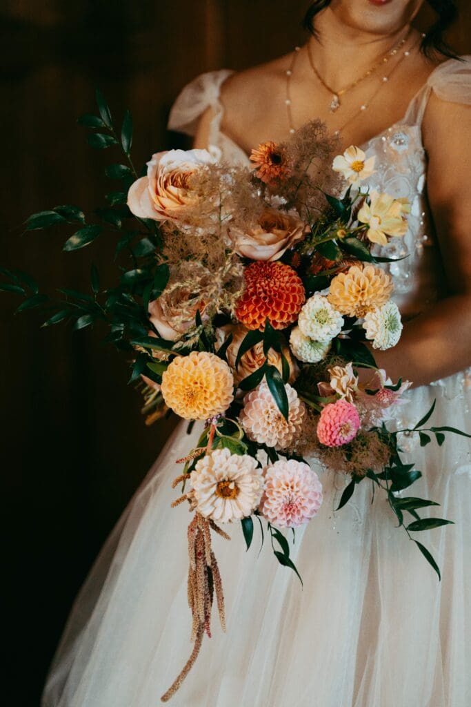 Bride holding a warm-toned wedding bouquet with toffee roses, ranunculus, and autumn accents