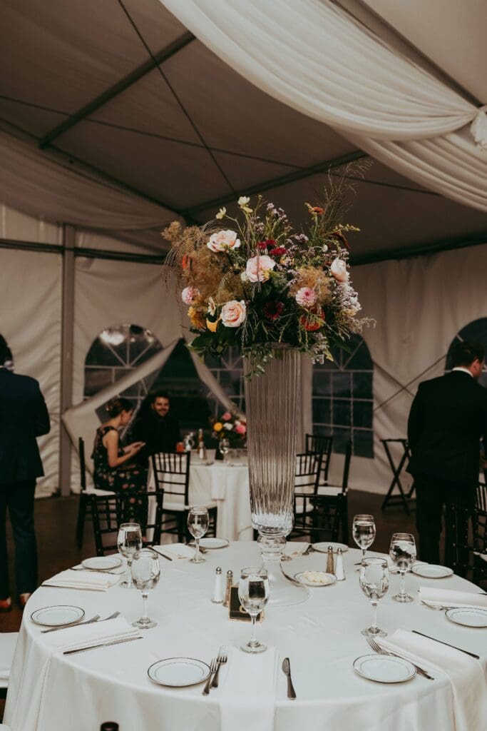 Tented reception setup with round tables and tall floral centerpieces repurposed from the ceremony