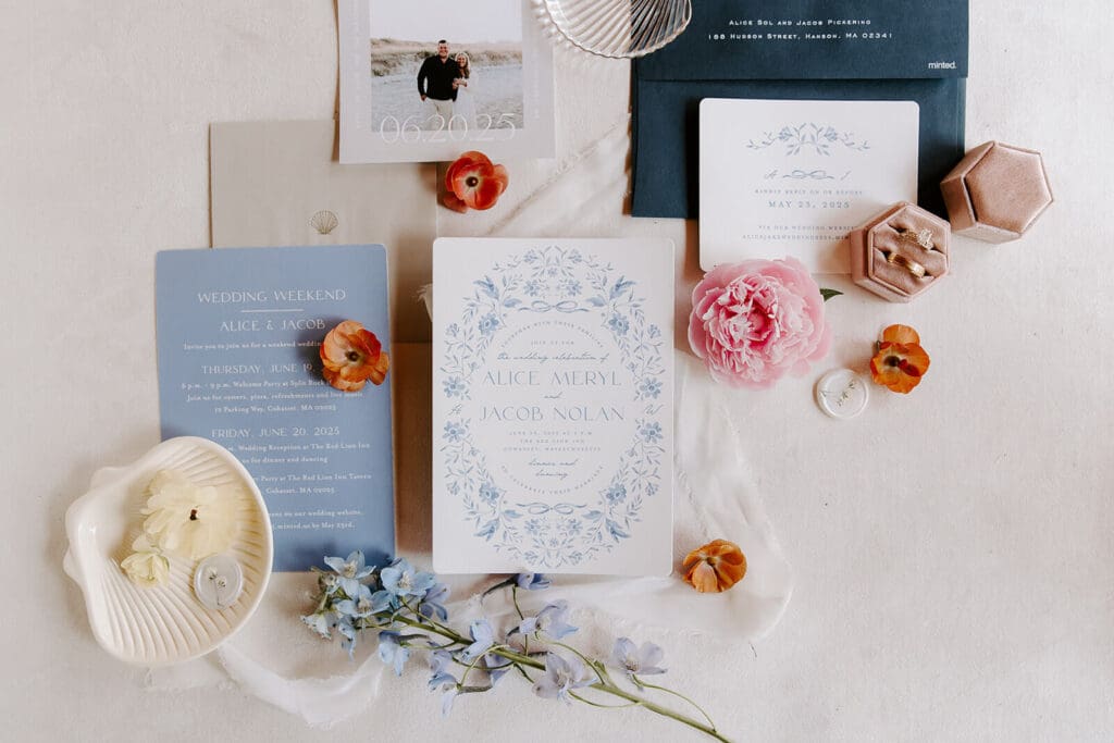 Flat lay of wedding invitations styled with seasonal flowers including delphinium, peonies, and ranunculus.