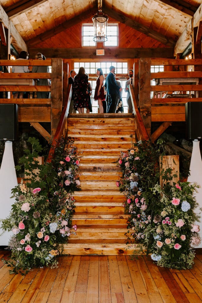Staircase installation at barn wedding venue covered with rustic wedding flowers including maple branches and hydrangea.