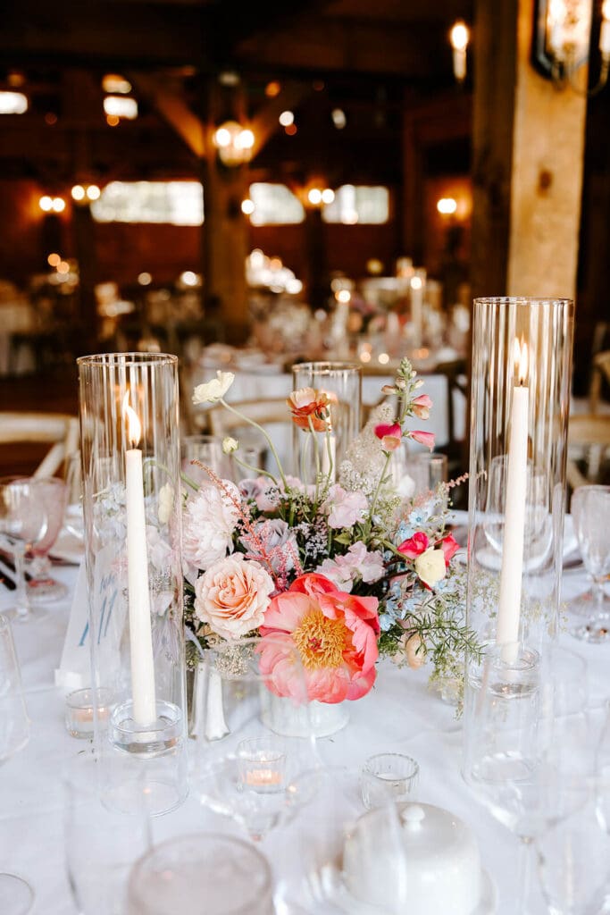 Modern bud vase centerpiece with seasonal flowers and tall taper candles at rustic barn wedding reception.