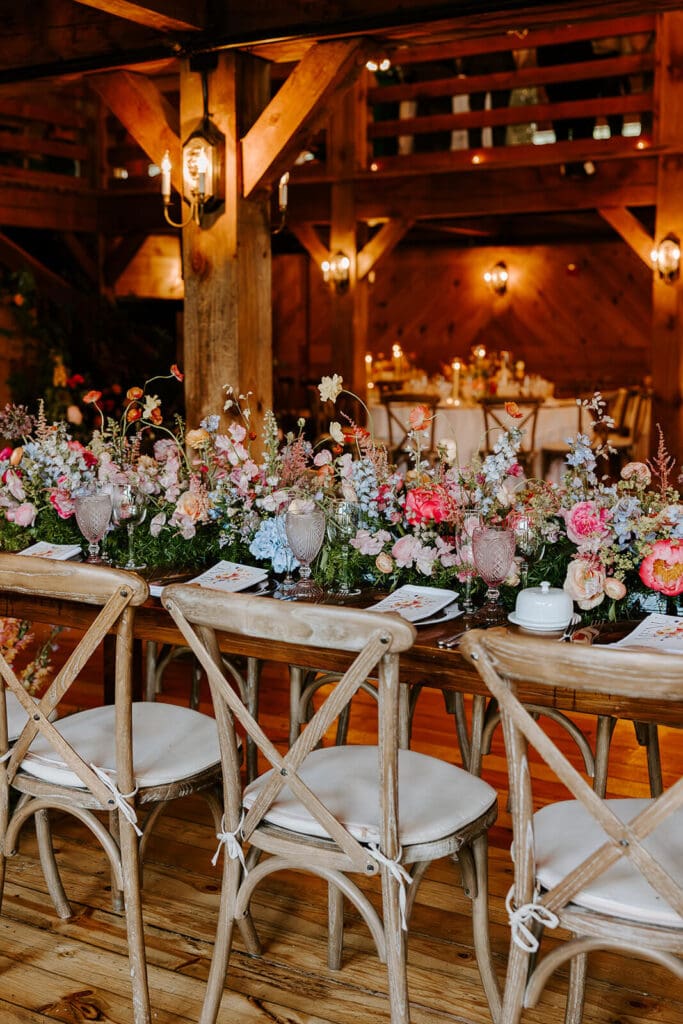 Rustic head table covered with garden-style seasonal flowers at barn wedding reception.