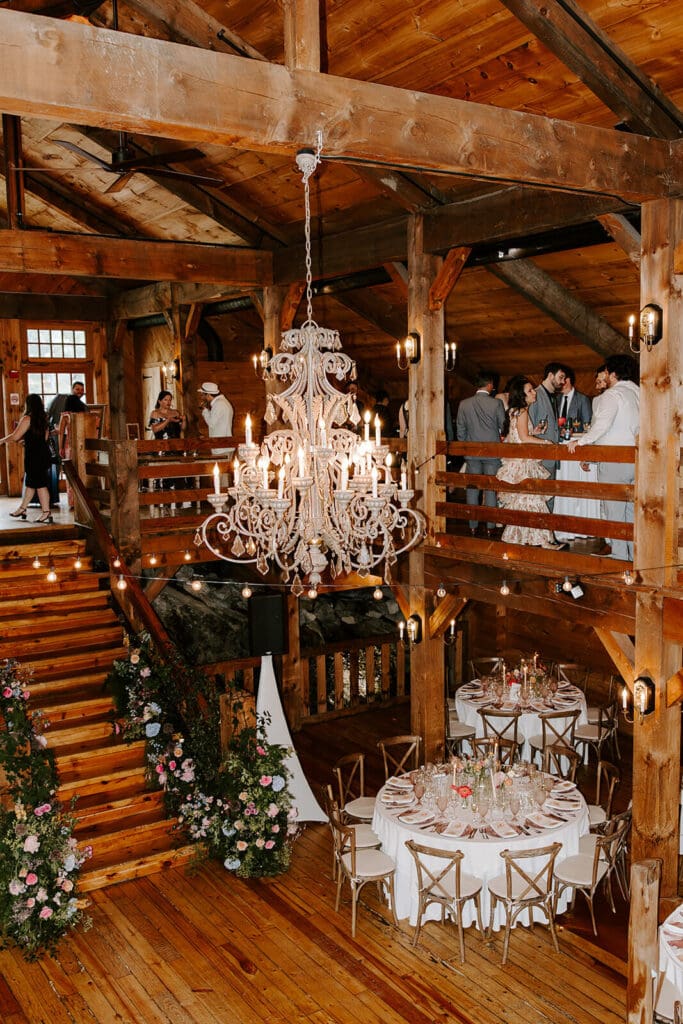 Barn wedding reception with rustic staircase floral installation and chandelier overhead.