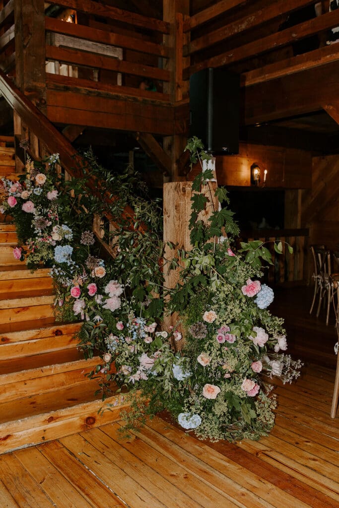 Close-up of rustic staircase installation with garden-style seasonal flowers at barn wedding venue.