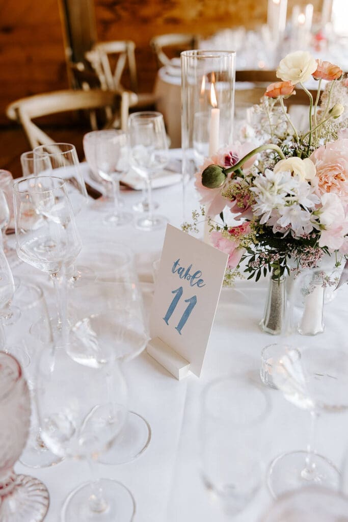 Barn wedding guest table centerpiece with seasonal flowers and modern glassware.