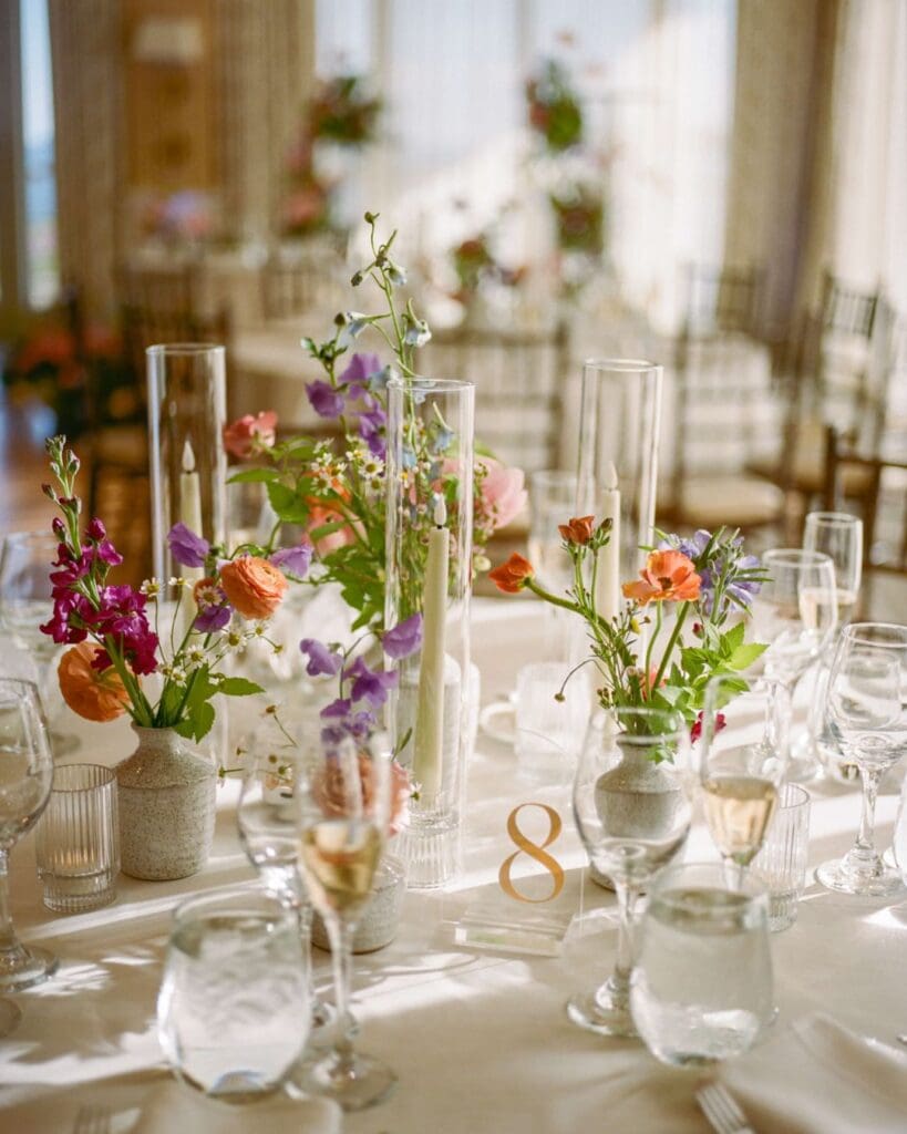 Reception room at the Beauport Hotel in Gloucester, with colorful seasonal flowers arranged on round tables for an oceanfront wedding celebration.