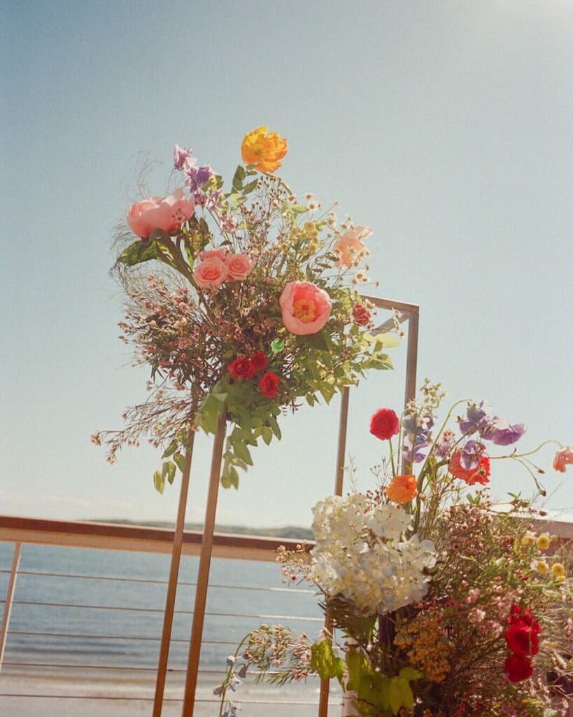 Beach wedding flowers in bold spring colors frame the Gloucester oceanfront view at a Beauport Hotel wedding ceremony.