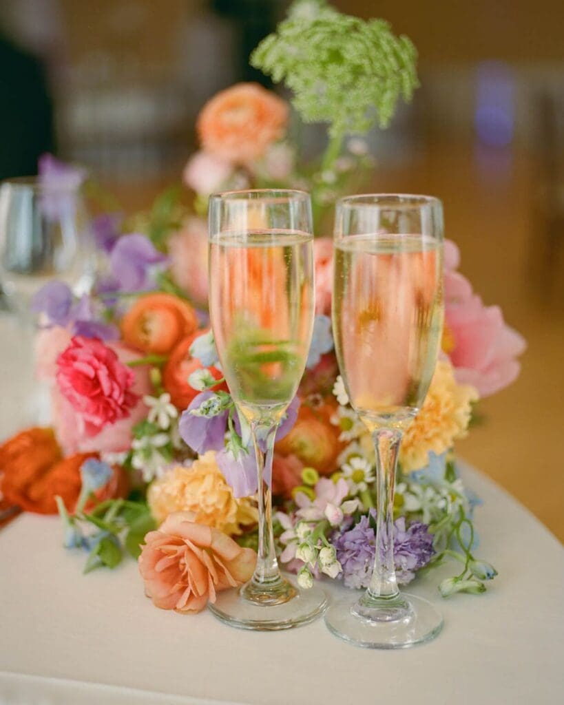 Champagne flutes in front of colorful spring flowers, celebrating a joyful Beauport Hotel Gloucester wedding by the sea.