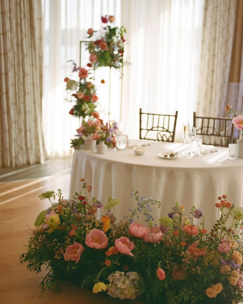 Sweetheart table framed by colorful wedding flowers, including pink peonies and hydrangea, for a vibrant spring Beauport Hotel Gloucester wedding.
