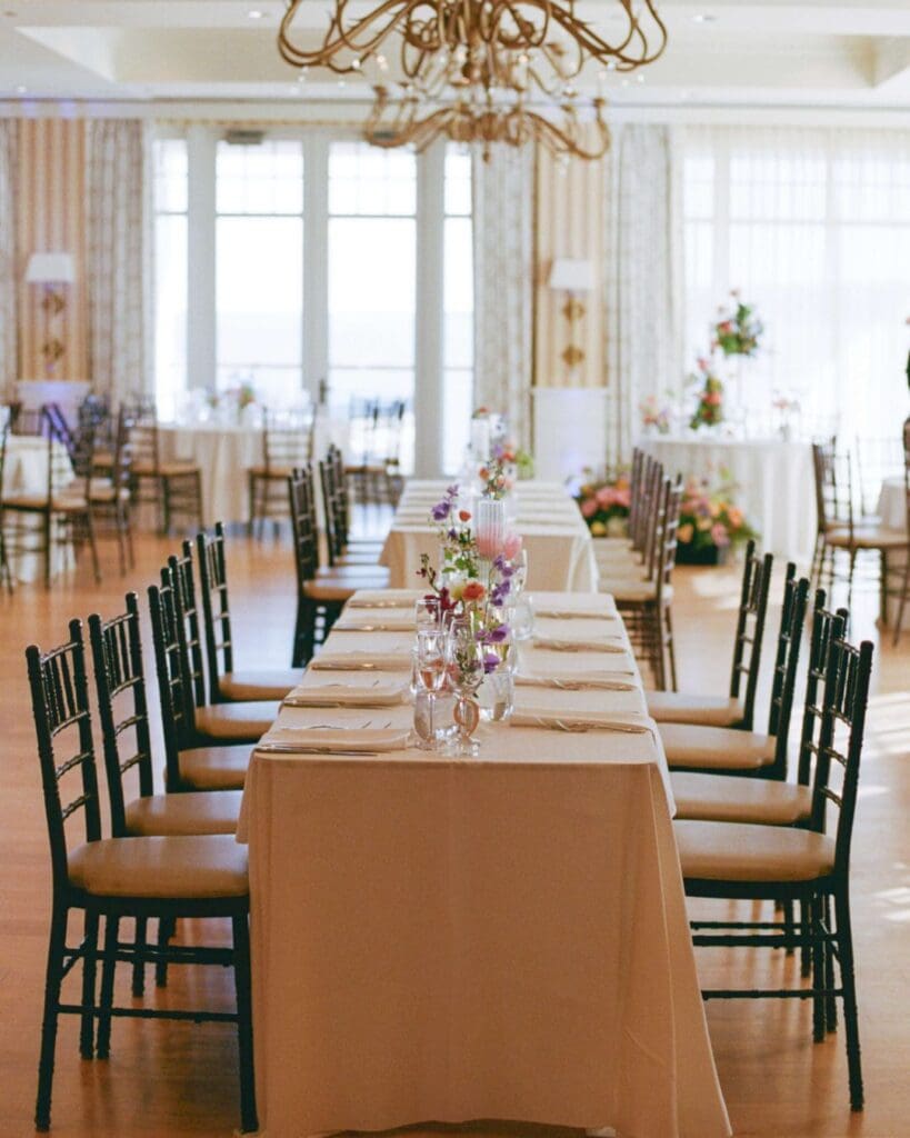 Banquet-style reception table decorated with colorful wedding flowers in bud vases, perfect for a modern Beauport Hotel Gloucester beach wedding.