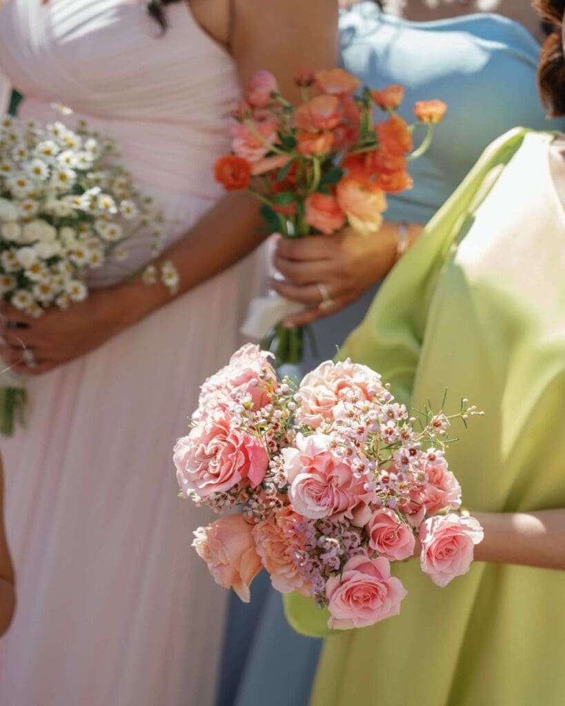 Bridesmaids in pastel gowns hold colorful wedding flowers, featuring pink spray roses, peach blooms, and daisy-like chamomile for a seasonal spring wedding in Gloucester.