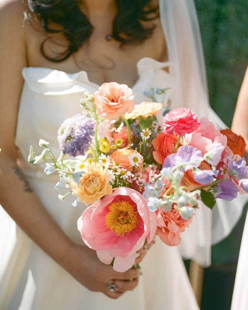 Close-up of a bright bouquet bursting with colorful wedding flowers—peonies, roses, ranunculus, sweet peas, and daisies—ideal for a spring beach wedding in Gloucester.