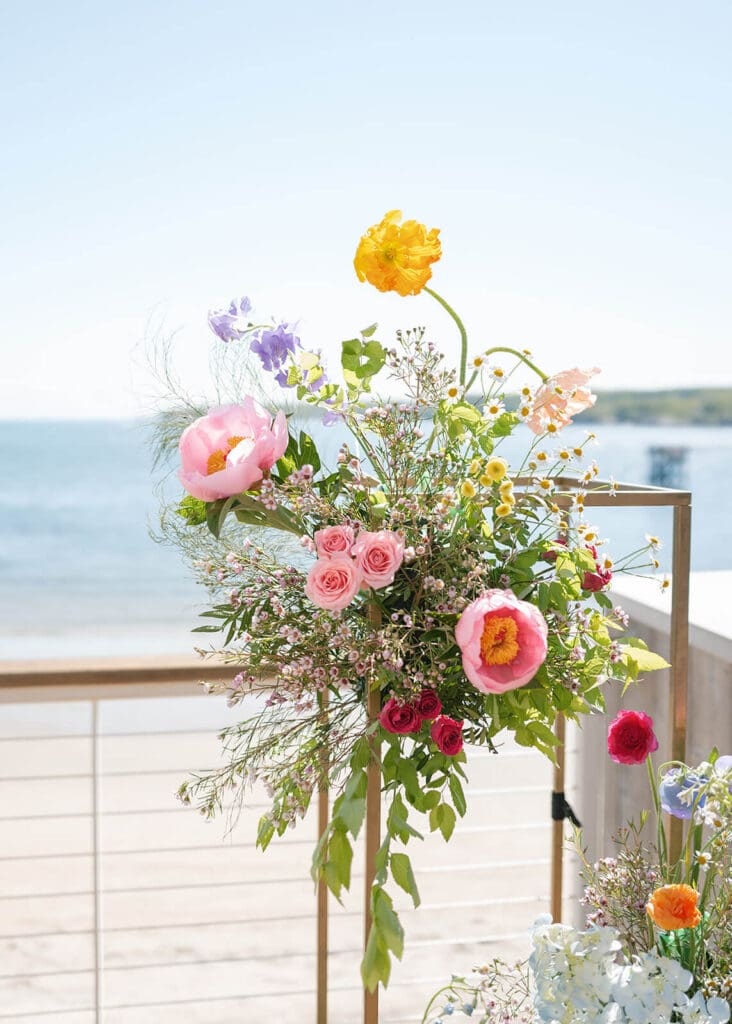 Beach wedding flowers in vibrant spring colors—yellow poppy, pink peonies, roses, and wild greenery—styled for a Beauport Hotel Gloucester ceremony.