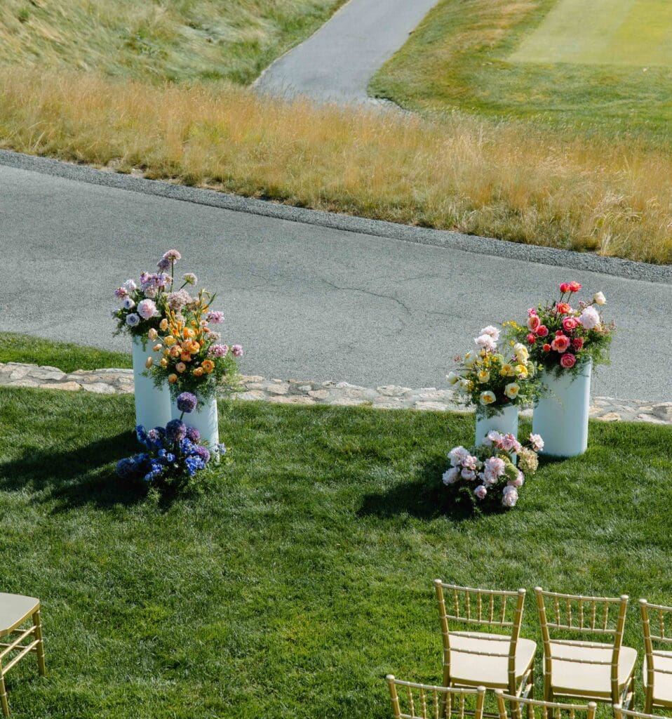White modern pedestals topped with colorful seasonal flowers overlooking the golf course at New Seabury Country Club, designed by Cape Cod wedding florist Rumphius Farms.