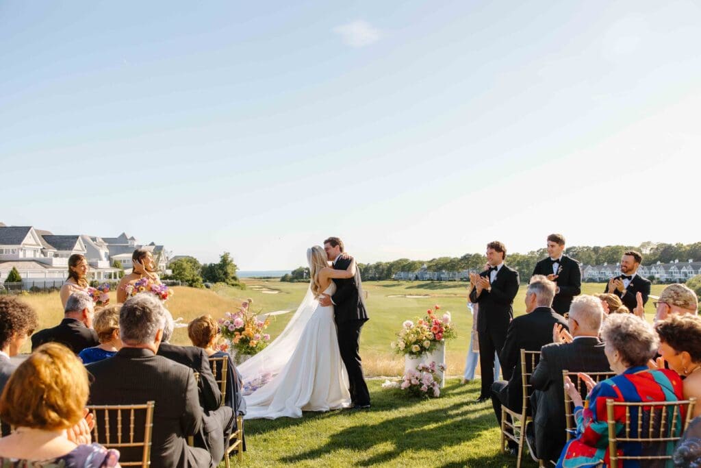 Bride and groom sharing their first kiss surrounded by colorful coastal wedding flowers at New Seabury Country Club on Cape Cod.