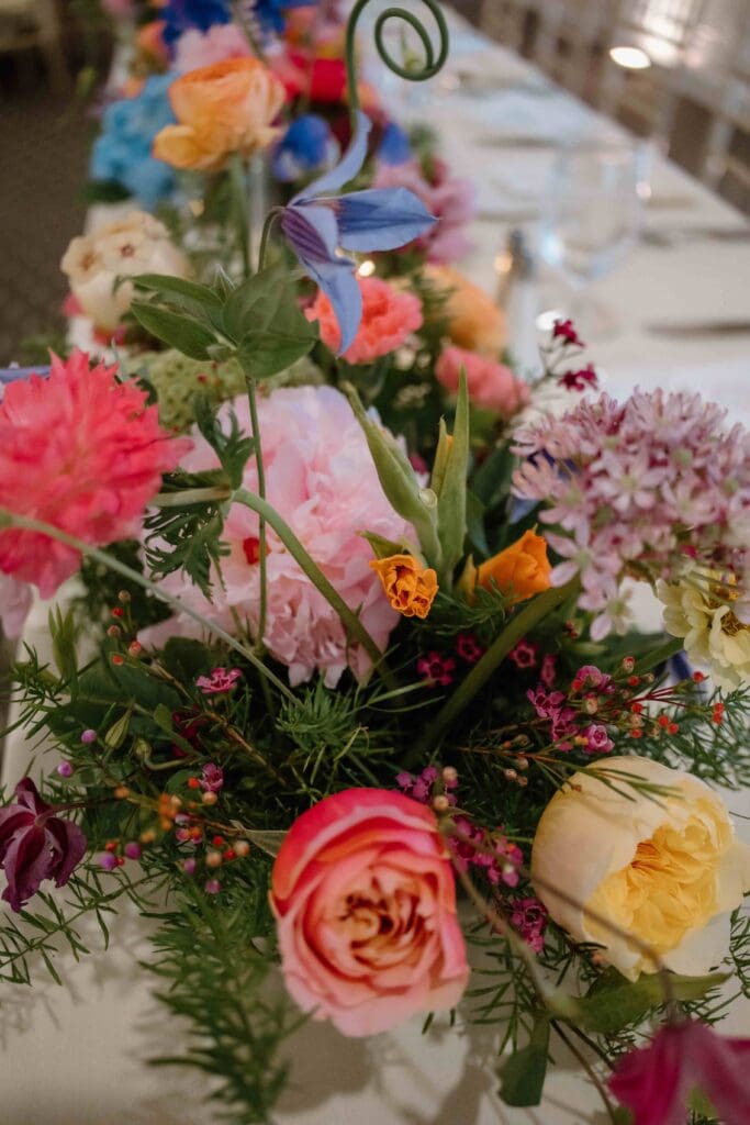 Long table at New Seabury Country Club styled with colorful garden-inspired arrangements, candlelight, and elegant gold chairs for a Cape Cod wedding.