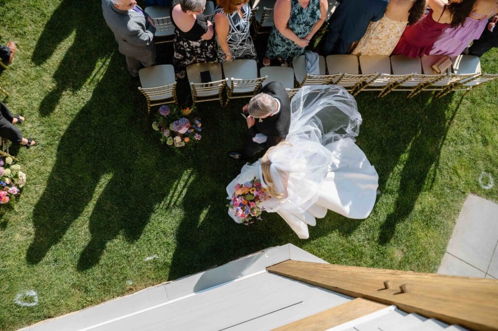 Aerial view of the bride walking down the aisle holding a modern wedding bouquet of colorful peonies and ranunculus at New Seabury Country Club.