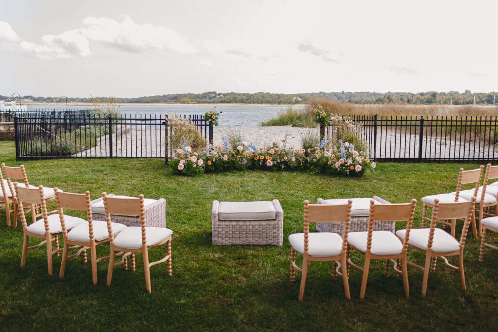 Wide view of the ceremony chairs arranged around the coastal meadow installation, overlooking the shoreline at an at-home Cohasset wedding.